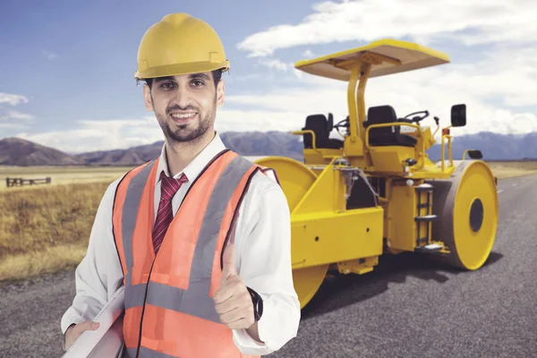 Engenheiro masculino usando capacete de segurança em pé na frente do rolo a vapor estacionado no local de construção da estrada — Fotografia de Stock