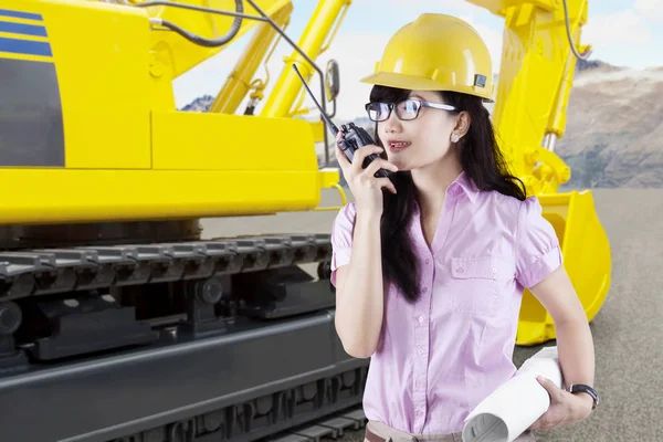 Vackra kvinnliga arkitekt talar med en walkie-talkie bredvid en traktor på en byggarbetsplats — Stockfoto