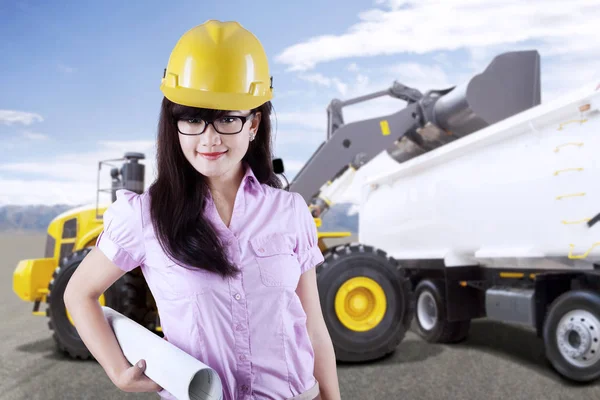 Female architect or contractor standing in front of an excavator loading truck with soil on a construction site — Stock Photo, Image