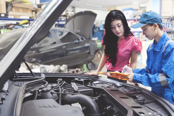 Mekanik mobil membantu seorang pelanggan berdiri di samping mobil yang diservis dan melihat melalui daftar cek . — Stok Foto