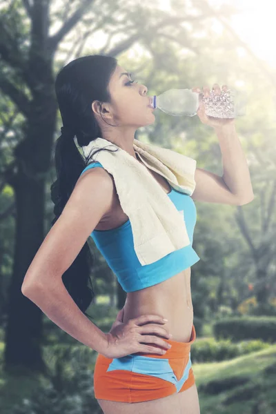 Beautiful slim woman with resting after jogging while drinking water at city park — Stock Photo, Image