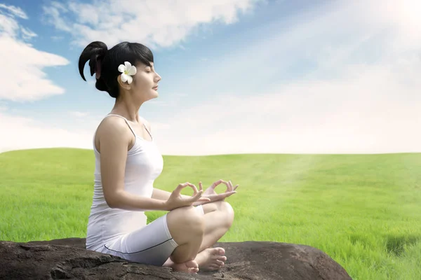 Femme asiatique méditant en plein air sur la roche à la prairie contre le ciel bleu — Photo