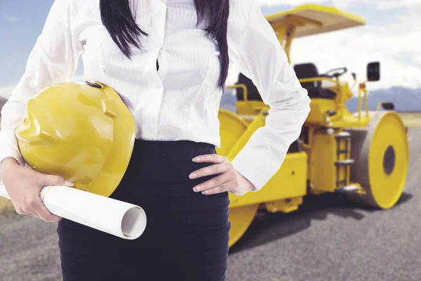 Anonymous female engineer holding a safety helmet standing in front of steamroller — Stock Photo, Image