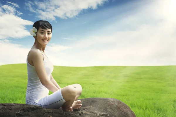 Asian woman enjoying outdoors sitting on the rock at meadow against blue sky Royalty Free Stock Photos