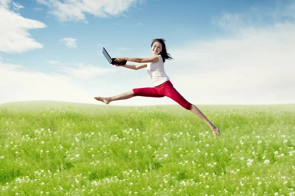 Asian woman ballerina holding laptop computer making a big jump on blossom meadow. — Stock Photo, Image