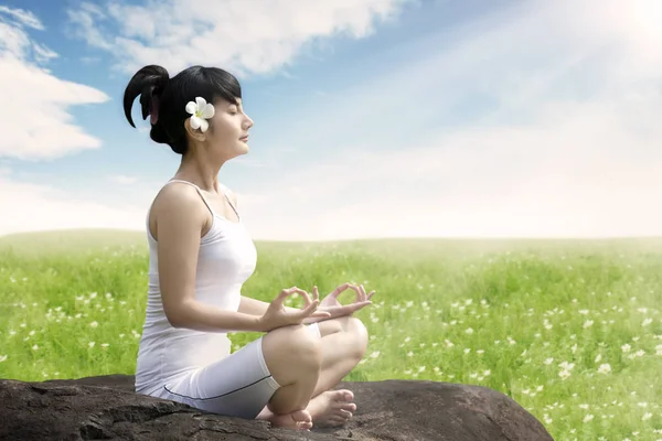 Mujer asiática meditando al aire libre en la roca en el prado contra el cielo azul —  Fotos de Stock