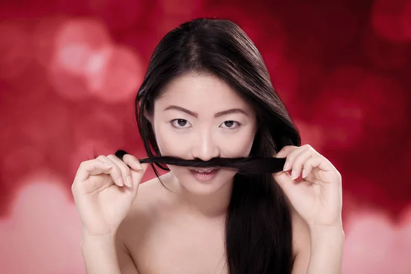 ぼやけた赤い背景の髪と遊ぶ美しい中国女性 — ストック写真