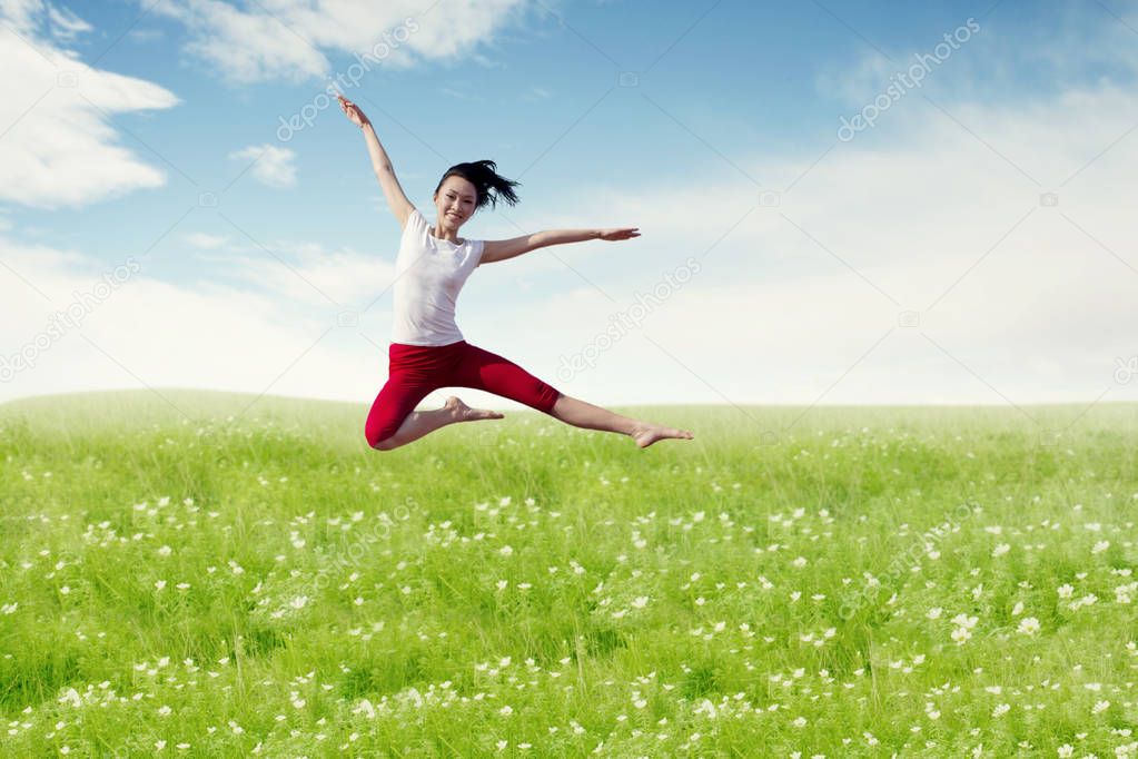 Asian woman ballerina making a big jump on meadow.