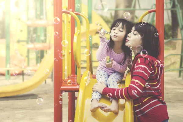 Moeder en dochter spelen zeepbellen op speelplaats. — Stockfoto
