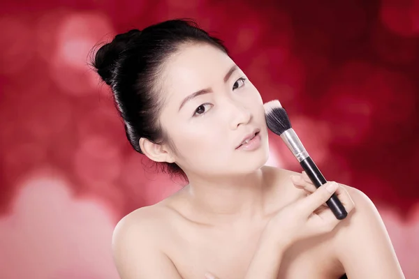 Beautiful oriental woman with flawless skin holding a makeup brush