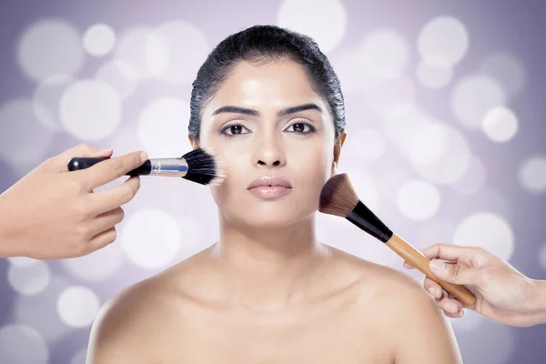 Vacker indisk kvinna med makeup borste mot suddig ljus bakgrund. — Stockfoto