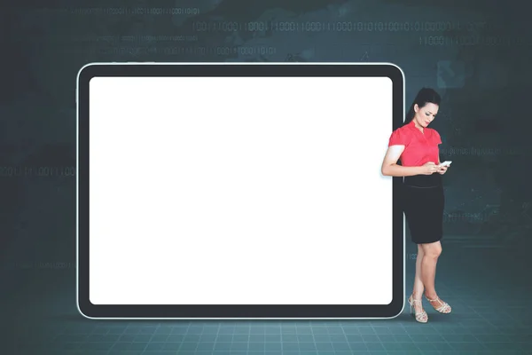 Businesswoman holding a digital tablet leaning on empty billboard
