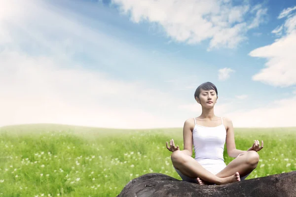 Mujer asiática meditando al aire libre en la roca en el prado contra el cielo azul — Foto de Stock