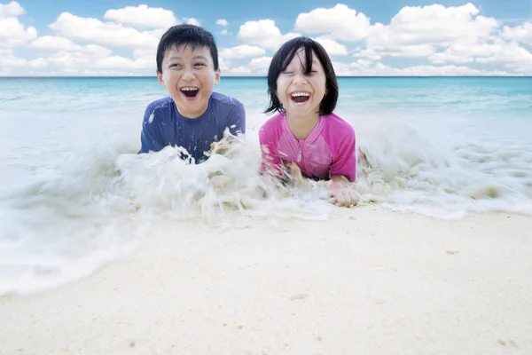 Två små barn spela vågor på stranden — Stockfoto