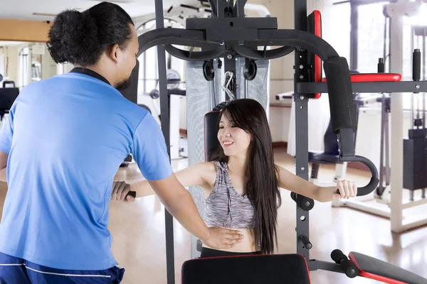 Trainer helping girl to exercise with weight machine — Stock Photo, Image