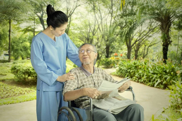 Stary człowiek rozmawia z jego pielęgniarka w parku — Zdjęcie stockowe