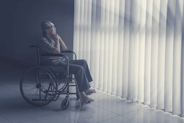 Задумчивый пожилой человек сидит на инвалидной коляске — стоковое фото