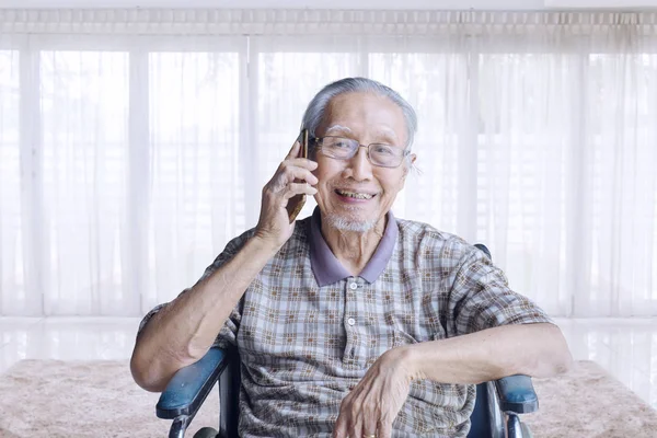 Старий розмовляє з мобільним телефоном на інвалідному візку — стокове фото