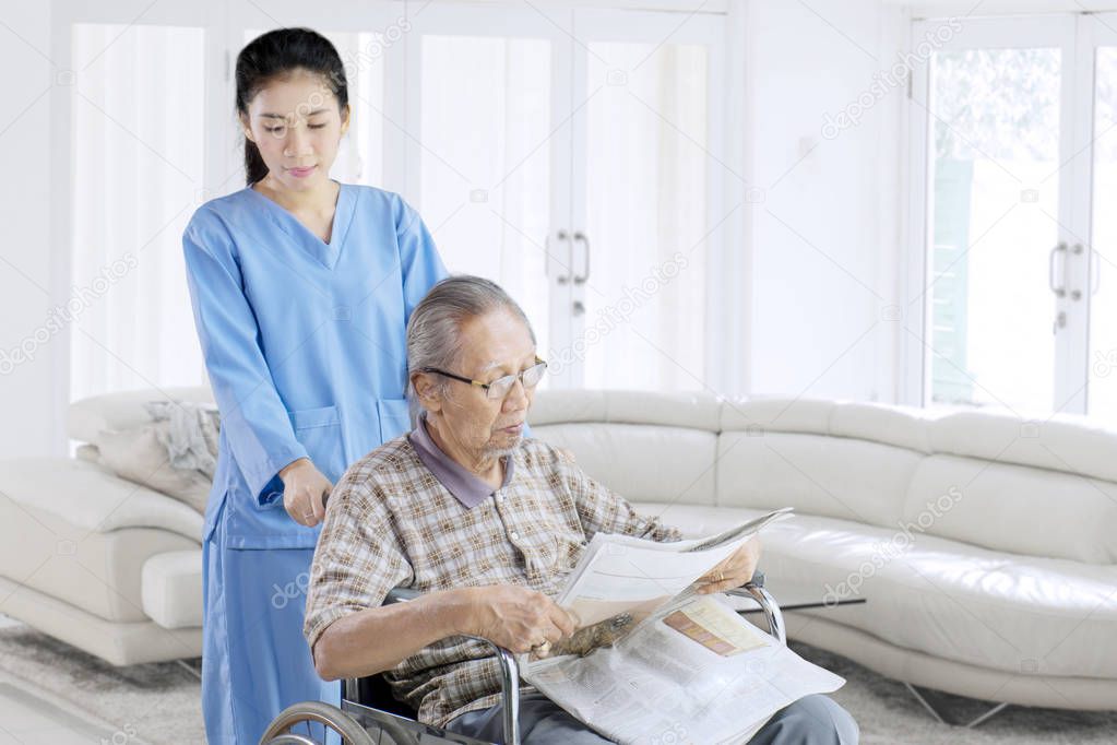 Old man reading newspaper with his nurse