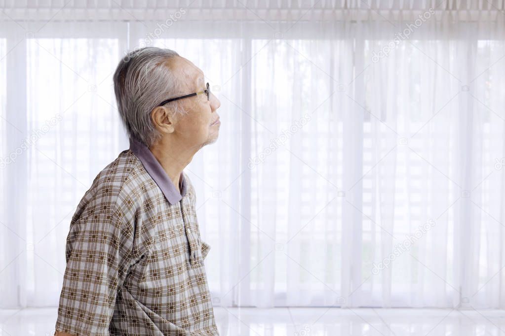 Lonely elderly man daydreaming near window