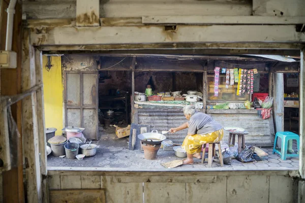 Stará žena vaření mimo její drobný obchod — Stock fotografie