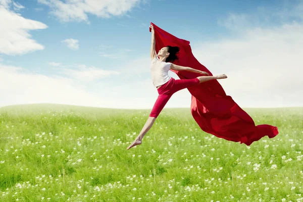 Азиатка-балерина, держащая красную ткань, совершила большой прыжок по цветущему лугу . — стоковое фото