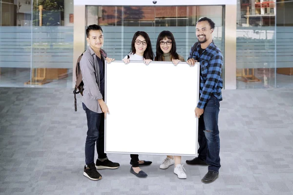 Grupo de estudiantes universitarios sosteniendo una pizarra blanca con espacio para copiar — Foto de Stock