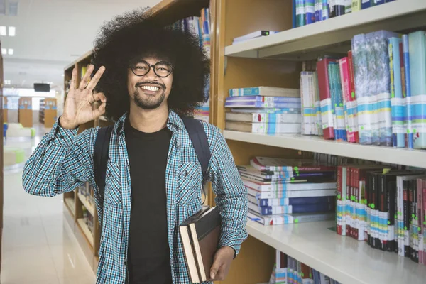 Студент-мужчина показывает знак ОК в библиотеке — стоковое фото