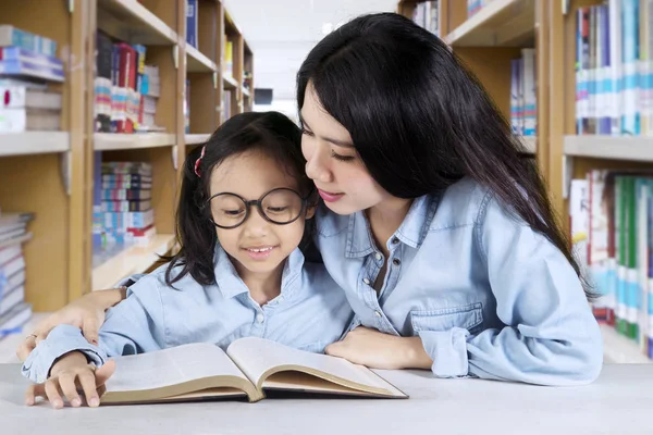 Маленькая девочка с учителем сидит в библиотеке — стоковое фото