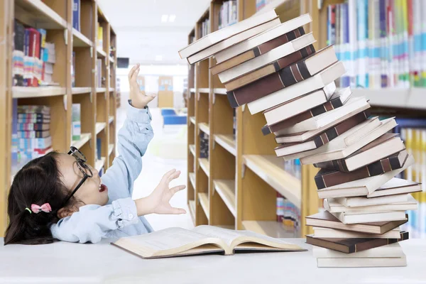 Liten flicka med högen av böcker i biblioteket — Stockfoto