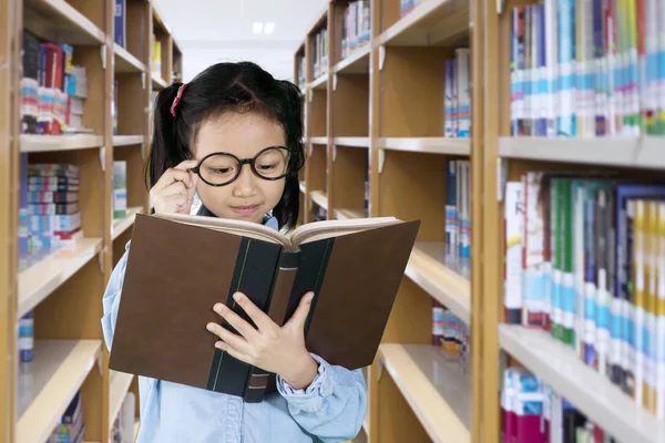 Little girl reading a textbook in the library — Stock Photo, Image