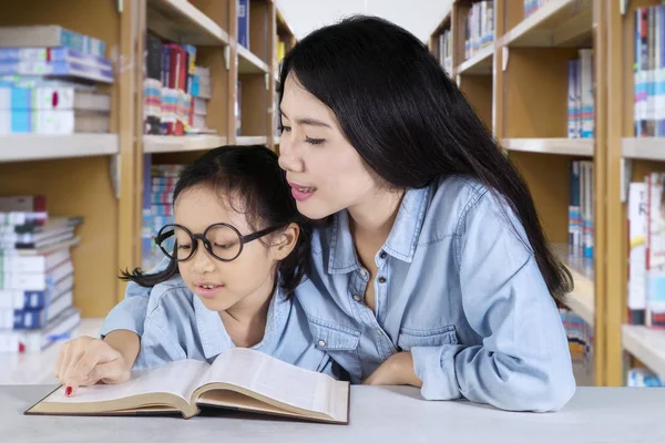 Милая школьница читает книгу со своим учителем — стоковое фото