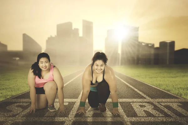 Two overweight women kneeling on the start line — Stock Photo, Image