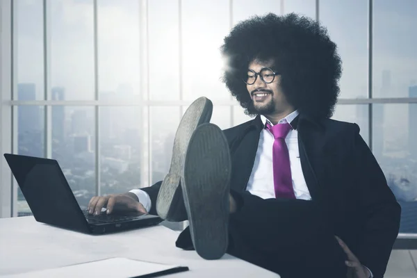 Afro-Amerikaanse zakenman met voeten op het bureau werken met laptop — Stockfoto