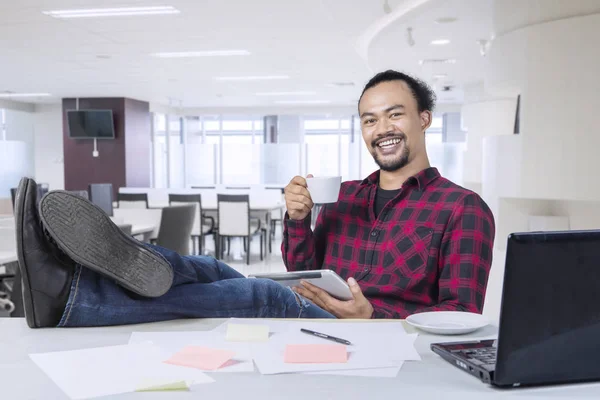 Happy professional worker with a cup of coffee and feet on desk