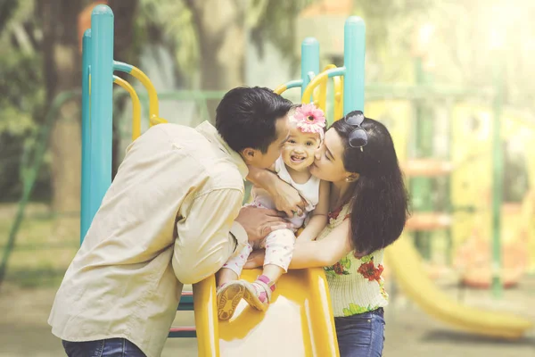 Pai e mãe beijando filha em slides — Fotografia de Stock