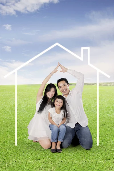 Ευτυχισμένη οικογένεια κάνοντας χέρι κατασκευασμένο σπίτι σε ένα λιβάδι — Φωτογραφία Αρχείου