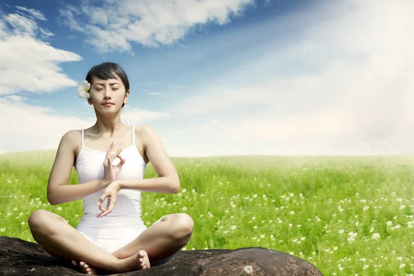 Mujer asiática meditando al aire libre en la roca en el prado contra el cielo azul —  Fotos de Stock