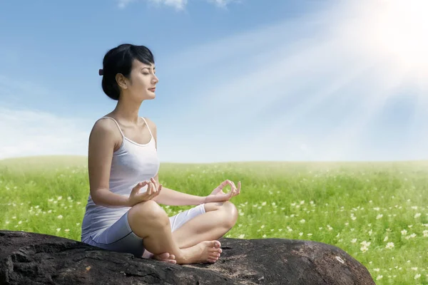 Mulher asiática meditando ao ar livre na rocha no prado contra o céu azul — Fotografia de Stock