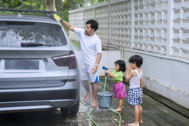 Genç bir adam onun çocukları ile bir araba bir sünger ile silerken yıkama görüntüsünü