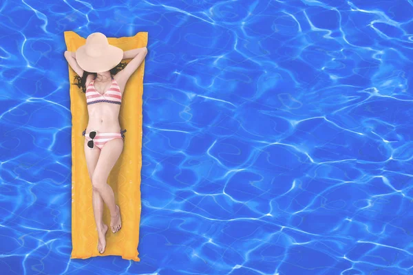 スイミング プールで黄色の空気マットレスの上のビキニを着てリラックスしたスリムな若い女性のトップ ビュー — ストック写真