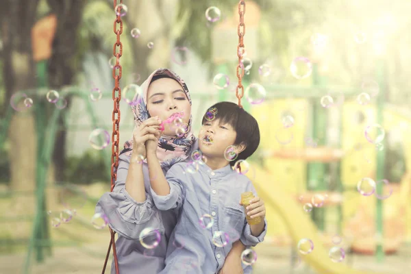 Mulher muçulmana sopra bolhas de sabão com seu filho — Fotografia de Stock