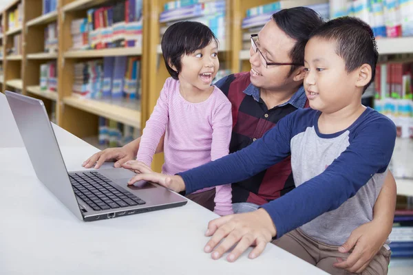 Padre e hijos estudiando con un ordenador portátil en una biblioteca — Foto de Stock