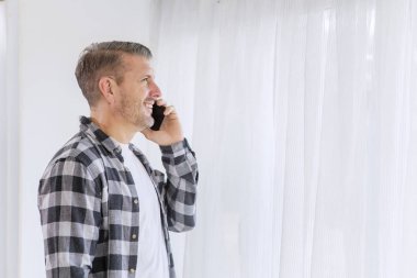 Pencerenin yanında telefonla konuşan mutlu bir adam.