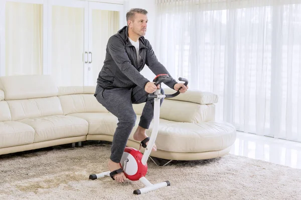 Uomo europeo che si esercita su una bici a pedalata assistita a casa — Foto Stock