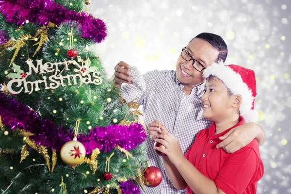 Pai e filho colocam ornamentos em uma árvore de Natal — Fotografia de Stock