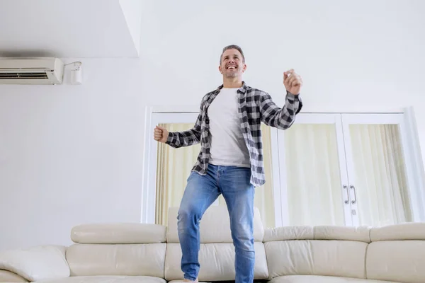 Visão de baixo ângulo de homem sorridente dançando no sofá — Fotografia de Stock