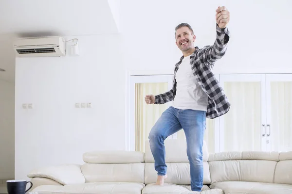 Зрелый мужчина танцует со счастливыми выражениями на диване — стоковое фото