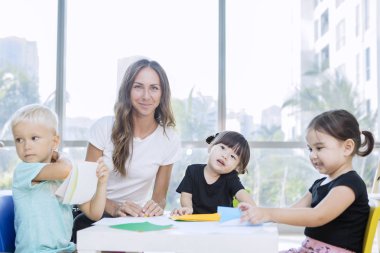 Anaokulu öğretmeni ve öğrencileri kağıt işi yapıyor.
