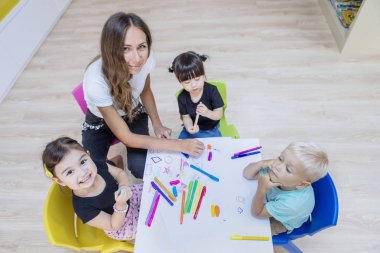 Kreş öğretmeni ve öğrenciler pastel boyalarla resim çiziyorlar. 
